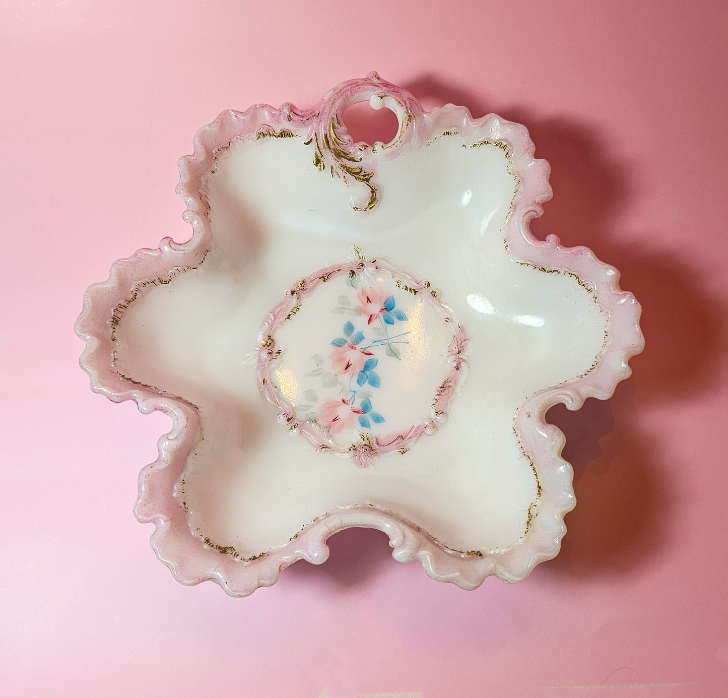 Decorative milk glass dish with floral design on a pink background