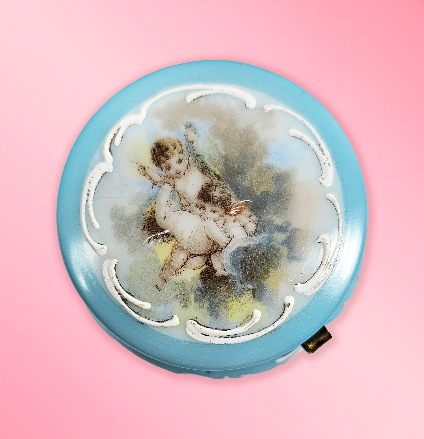 Round decorative item with cherub design on a pink background