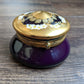 Purple jar with a gold lid featuring floral designs on a wooden surface