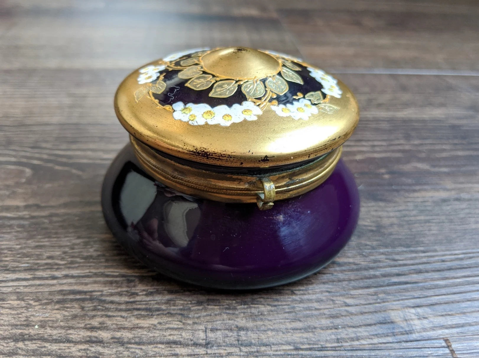 Purple jar with a gold lid featuring floral designs on a wooden surface