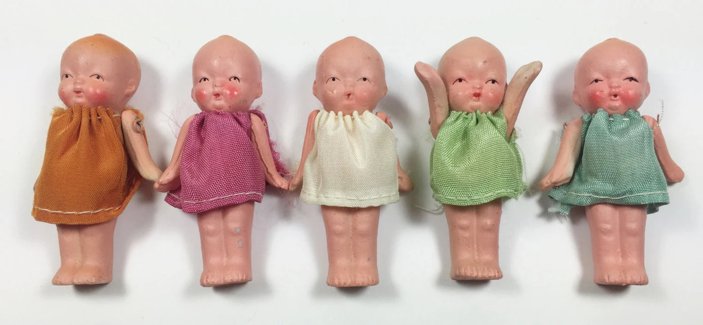 Five small dolls in colorful dresses lined up on a white background