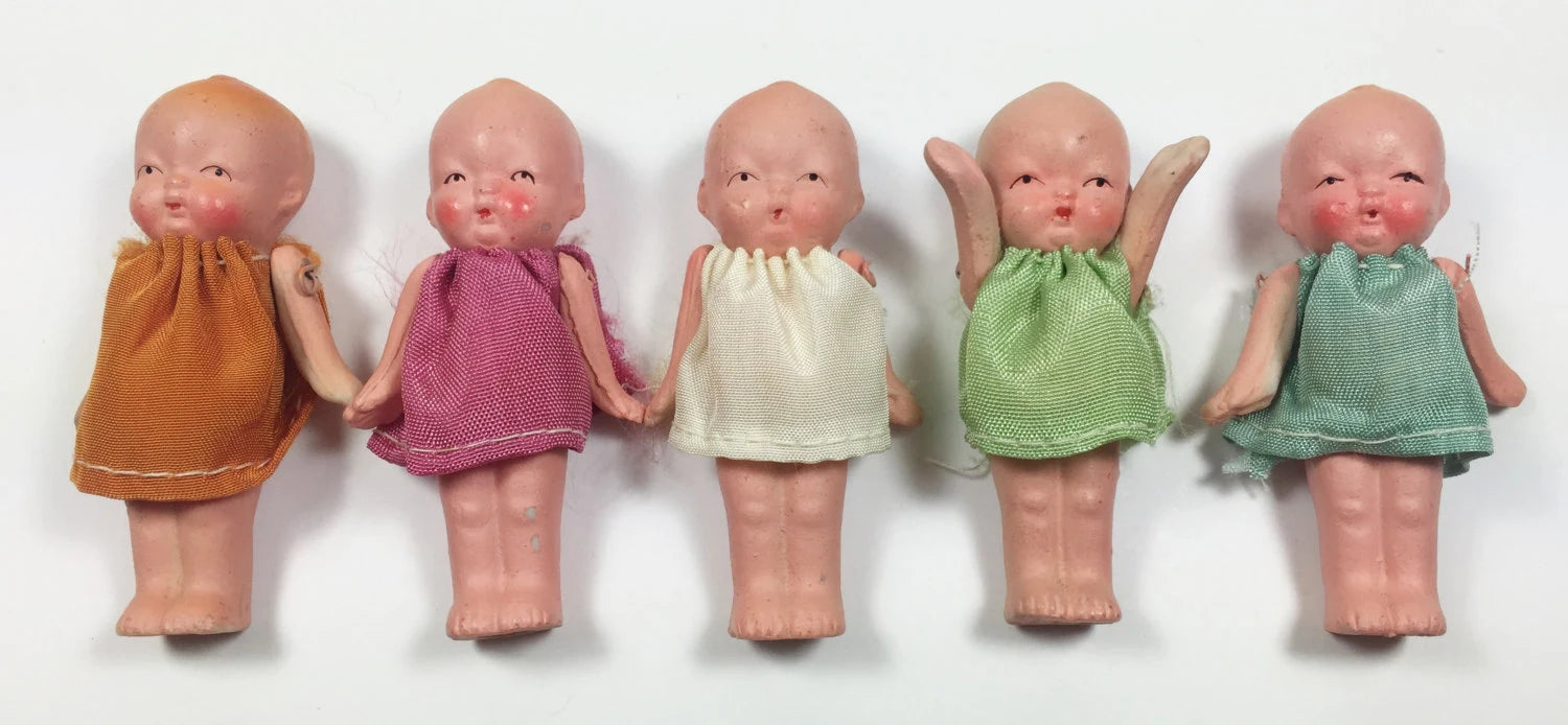 Five small dolls in colorful dresses lined up on a white background