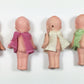 Five small dolls in various colored dresses lined up next to a ruler on a white background