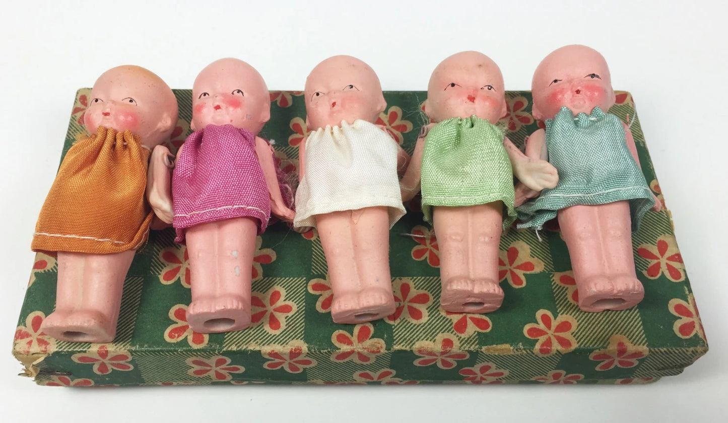Five small dolls with different colored dresses on a floral-patterned box.