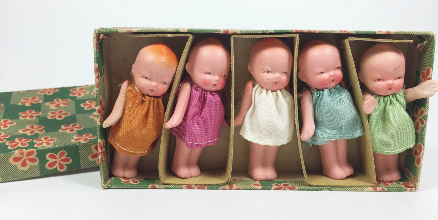 Five small dolls in colorful dresses inside a decorative box on a white background