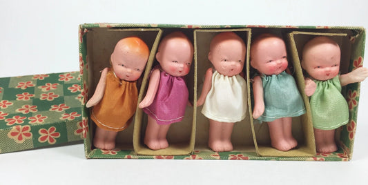 Five small dolls in colorful dresses inside a decorative box on a white background